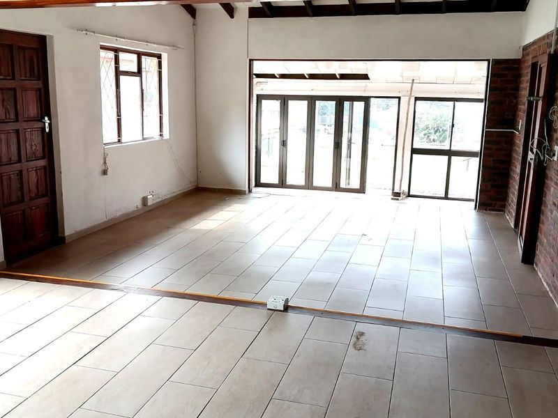 Spacious, empty living area featuring exposed brick walls, tiled flooring, and exposed timber ceiling beams, with large sliding glass doors leading to the exterior.