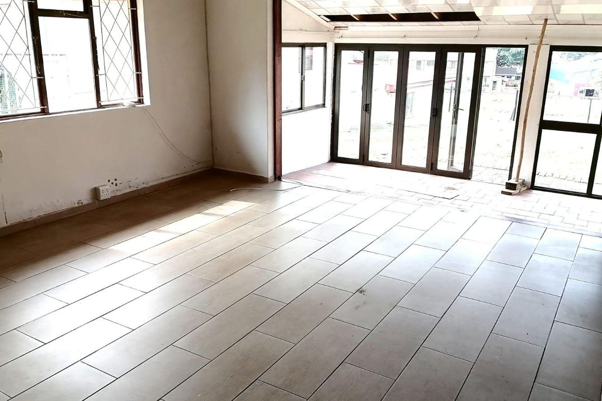An empty, open-plan living area featuring tiled flooring and large aluminium-framed folding doors that provide access to the outdoor space.