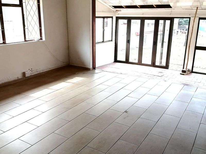 An empty, open-plan living area featuring tiled flooring and large aluminium-framed folding doors that provide access to the outdoor space.
