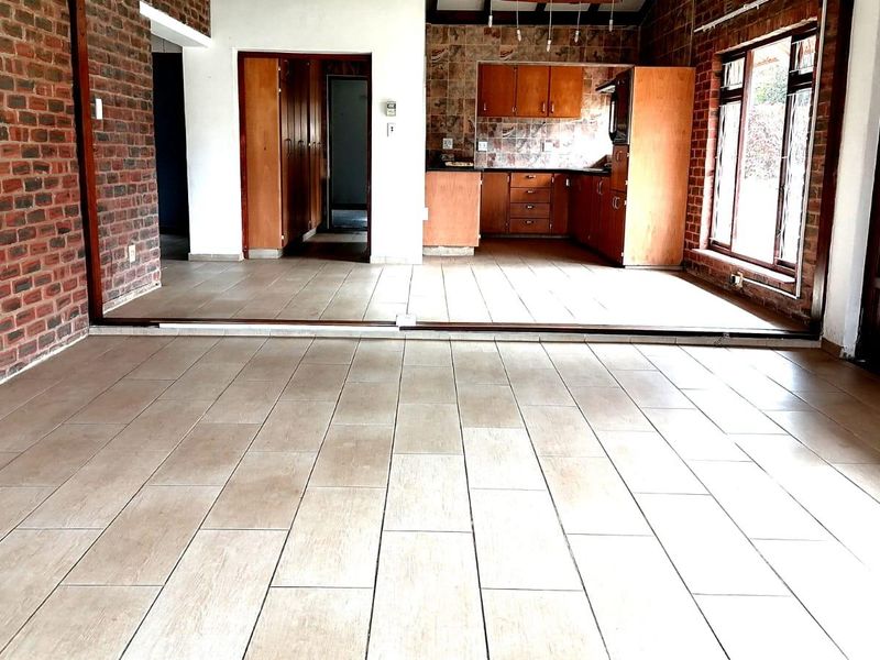 Spacious open-plan living and kitchen area featuring exposed brick walls, ceramic floor tiling, and traditional wooden cabinetry in the kitchen.