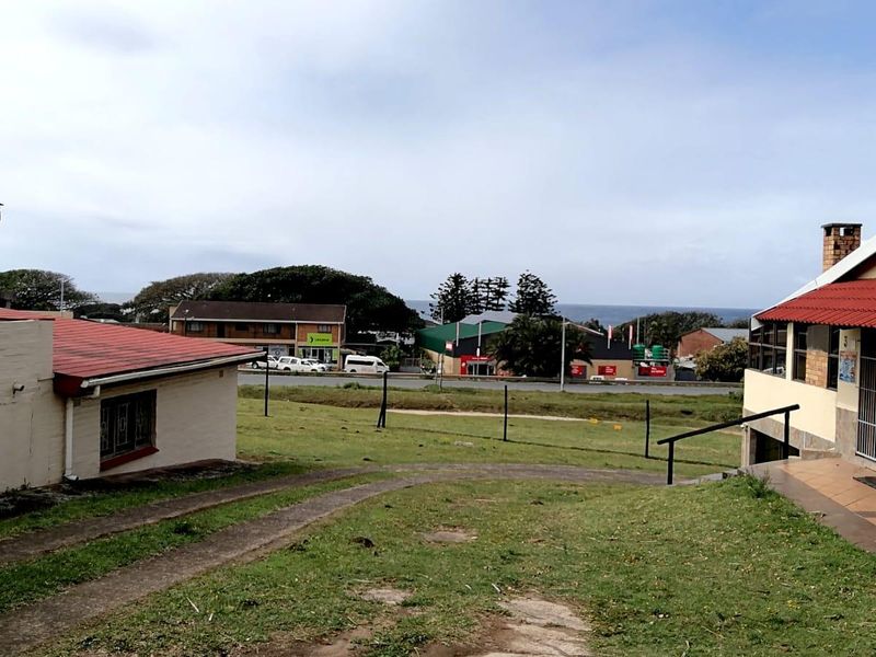 Rear view of the townhouse property showing the garden area, paved pathways, and surrounding neighbourhood with distant sea views.