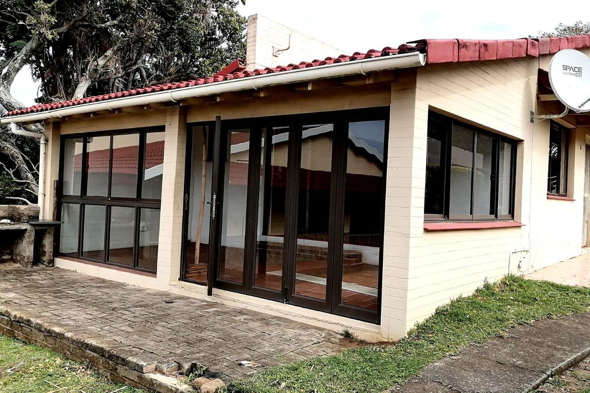 Rear exterior view of the townhouse featuring a paved patio area, built-in brick braai, and modern aluminium folding doors leading into the living space.