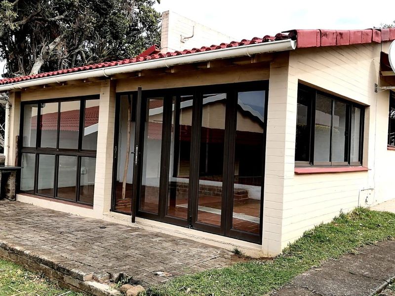 Rear exterior view of the townhouse featuring a paved patio area, built-in brick braai, and modern aluminium folding doors leading into the living space.