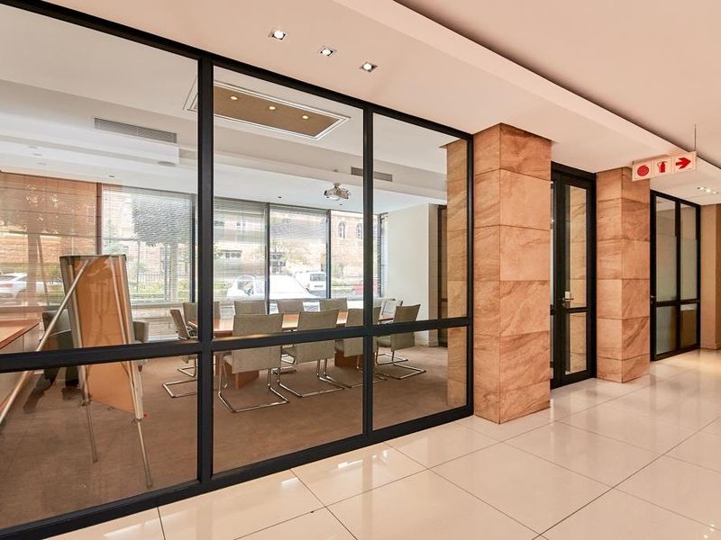 Modern office space featuring a glass partition wall, polished tiled flooring, and a stone-clad pillar in a well-lit, professional commercial environment.