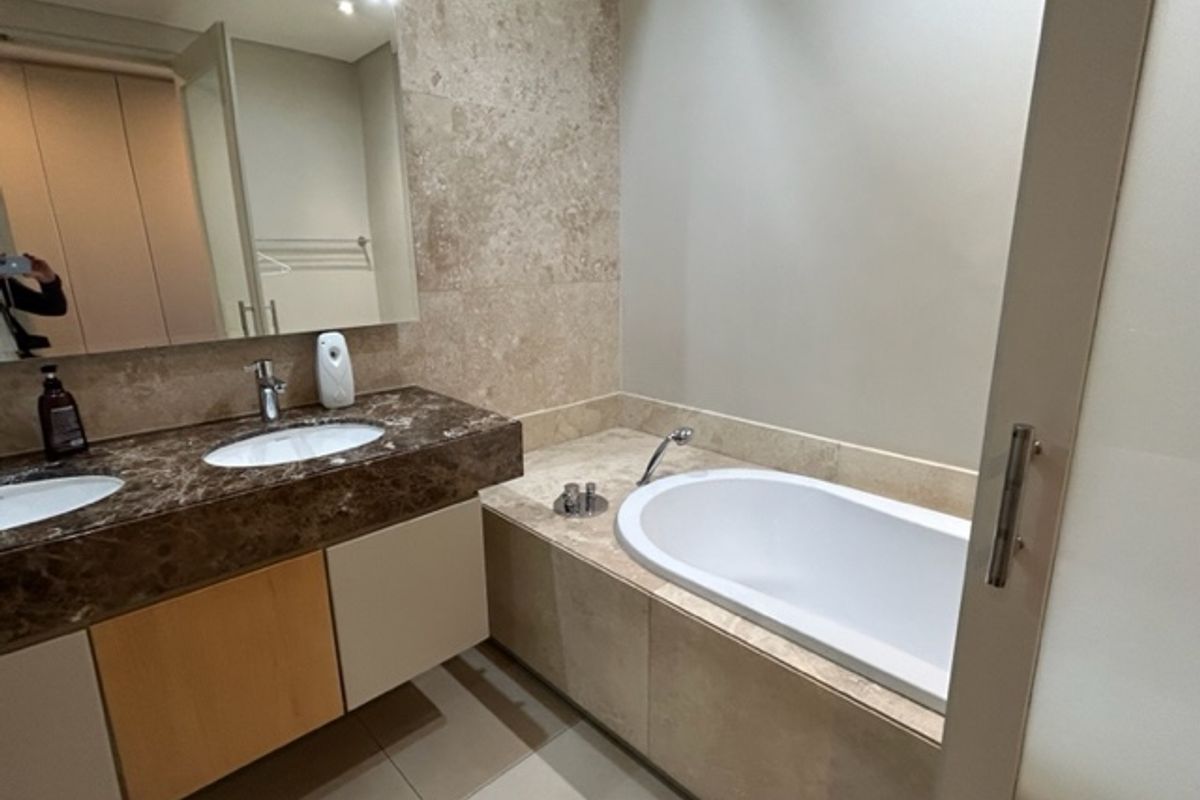 A modern bathroom featuring a double vanity with stone countertops, built-in bathtub, and neutral tiled finishes throughout.
