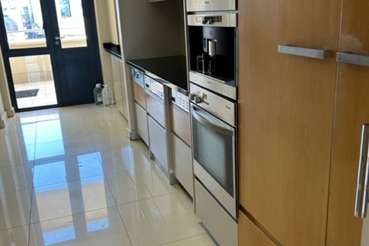 Modern kitchen featuring high-end integrated appliances, sleek cabinetry, stone countertops, and polished tiled flooring, leading to an outdoor balcony area.