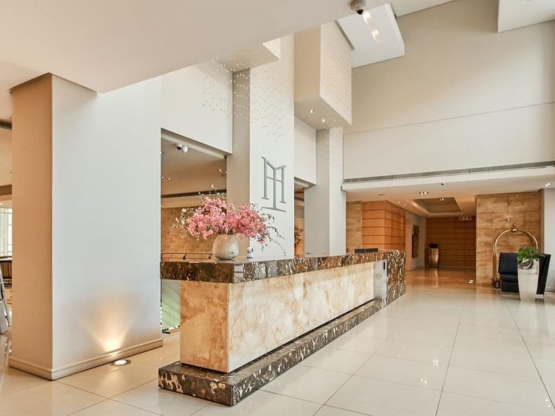 A modern, high-ceilinged apartment building lobby featuring a polished marble reception desk and bright, clean tiled flooring.