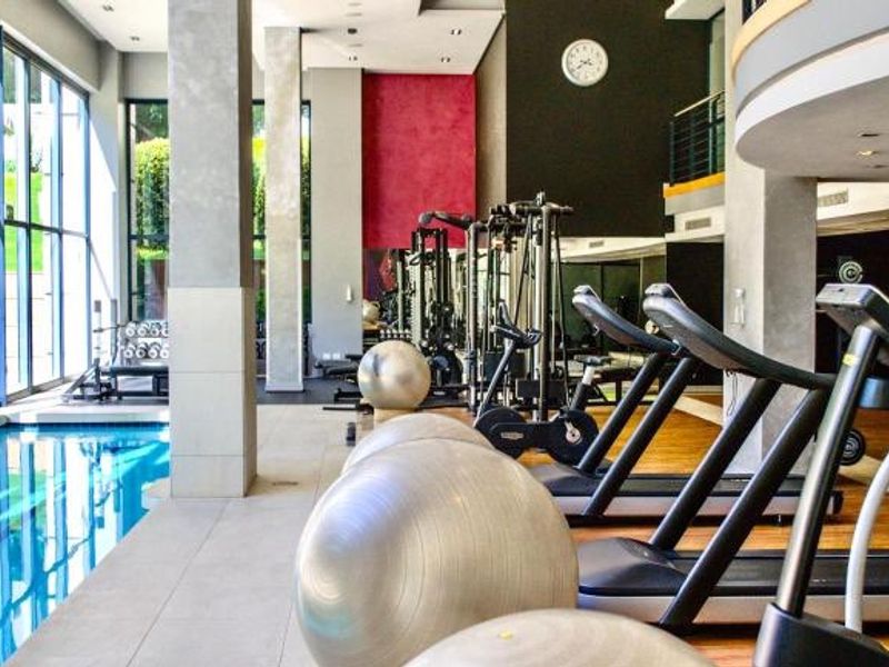 A modern, well-equipped indoor gym featuring a lap pool, floor-to-ceiling windows, and high-quality finishes, providing a bright and professional fitness environment.