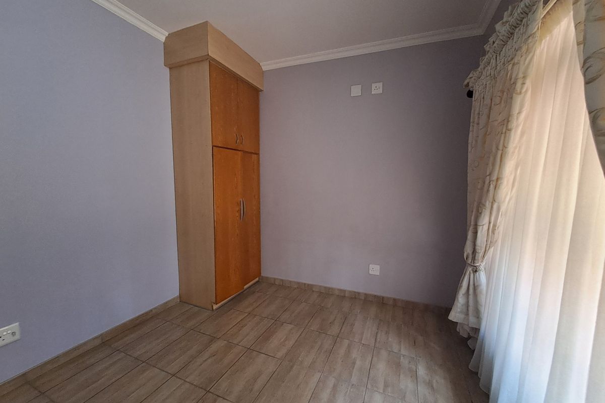 A clean, empty bedroom featuring tiled flooring, neutral wall paint, and a built-in wooden wardrobe.