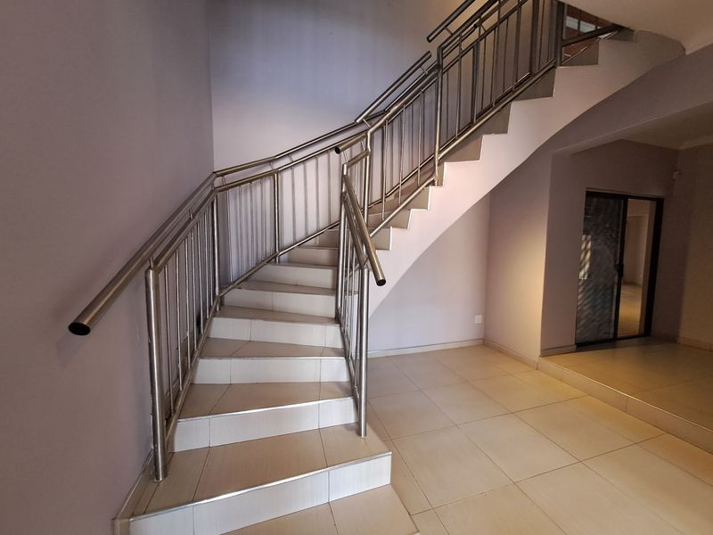 A bright, open hallway featuring a tiled staircase with a modern stainless steel balustrade and neutral wall finishes.