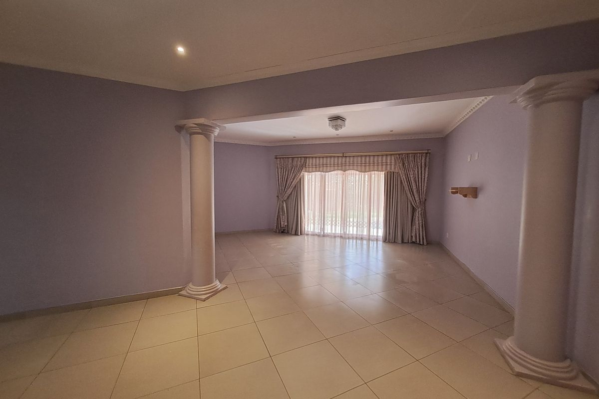 Spacious, open-plan living area featuring decorative columns, neutral tiled flooring, and large sliding glass doors providing natural light.