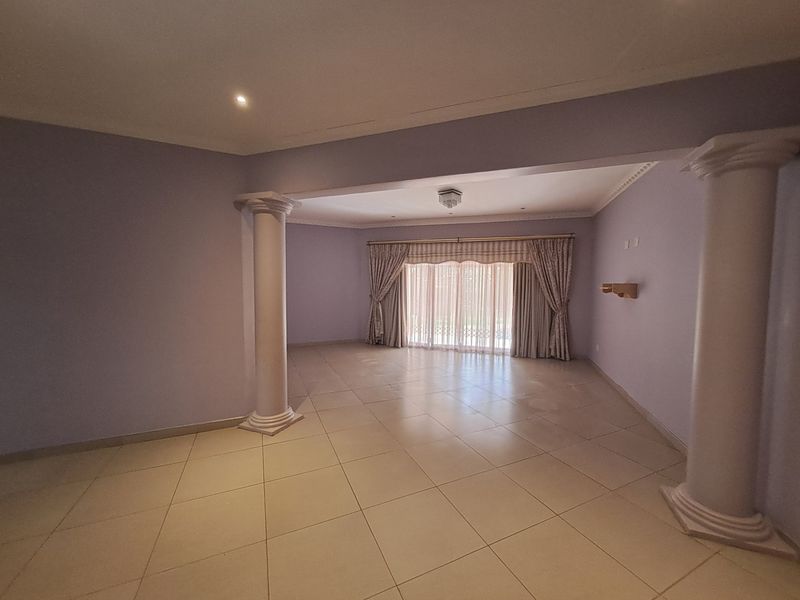 Spacious, open-plan living area featuring decorative columns, neutral tiled flooring, and large sliding glass doors providing natural light.