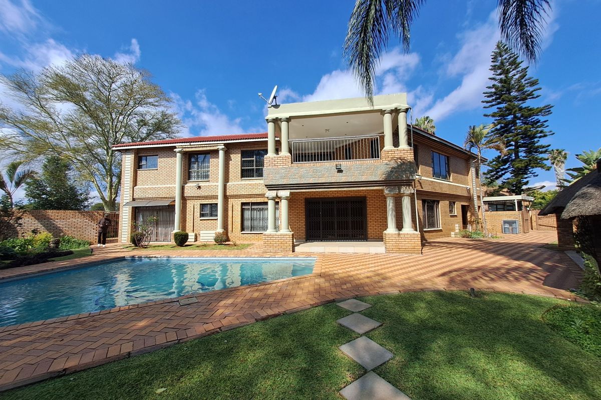 Rear view of a double-story brick house featuring a swimming pool, paved patio area, and an upper-level balcony with decorative columns.