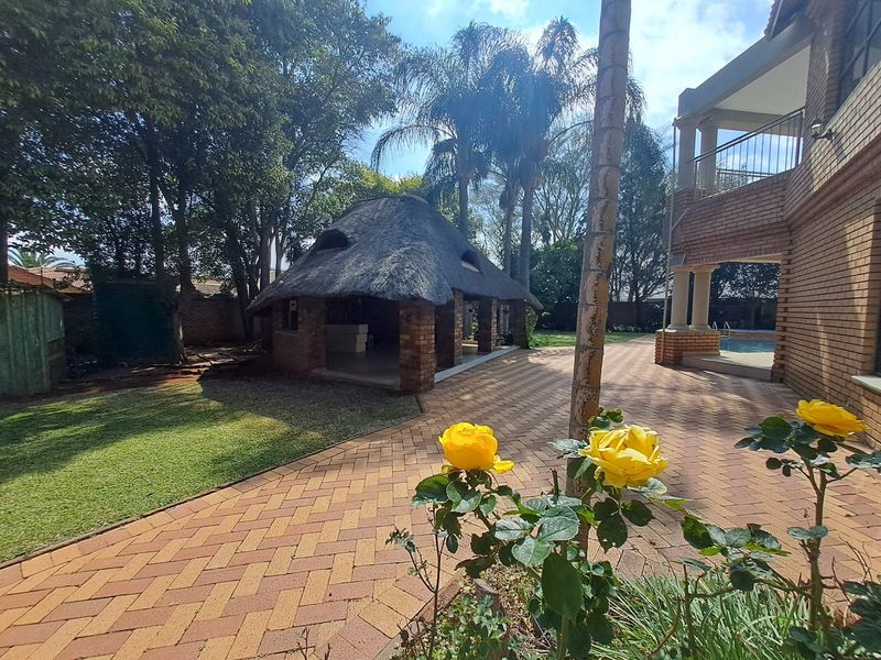 A spacious rear garden featuring a traditional thatched lapa, extensive brick paving, and a swimming pool adjacent to the main house structure.