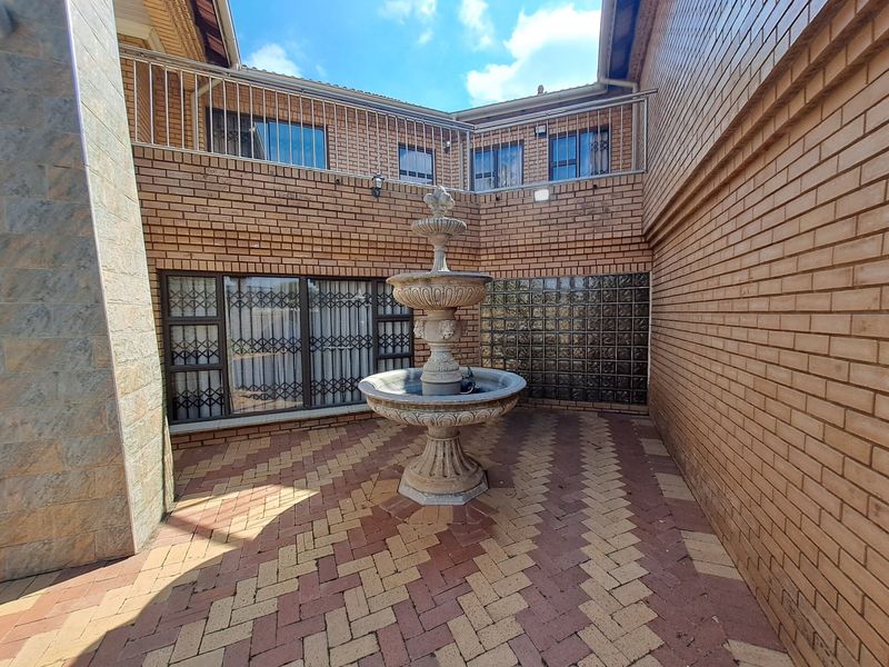 A private courtyard patio featuring decorative brick paving, a central stone fountain, and a unique glass block wall, enclosed by face brick architecture.