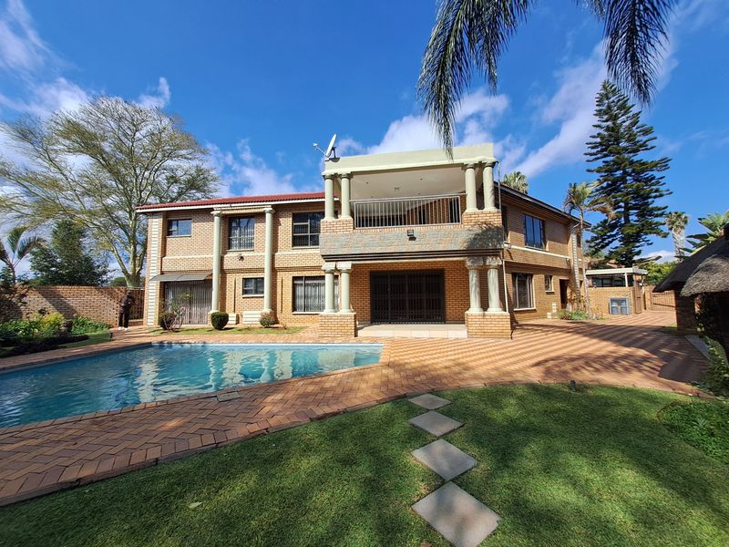 Rear view of a double-story brick house featuring a swimming pool, paved patio area, and an upper-level balcony with decorative columns.
