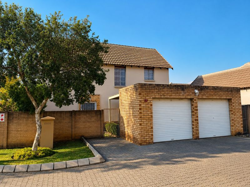 Front view of a townhouse featuring a double garage, paved driveway, and secure boundary wall with a tiled roof structure.