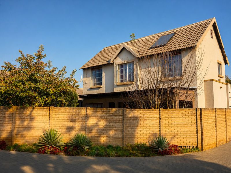 Front exterior view of a two-story townhouse featuring a tiled roof with solar panel, security bars on windows, and a brick boundary wall.