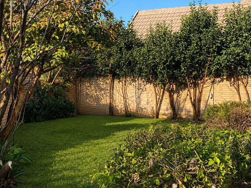 A private rear garden featuring a well-maintained lawn, mature trees, and a solid brick boundary wall.