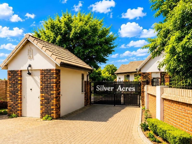 The entrance to Silver Acres complex featuring a secure gated access point, brick boundary walls, and paved driveway.