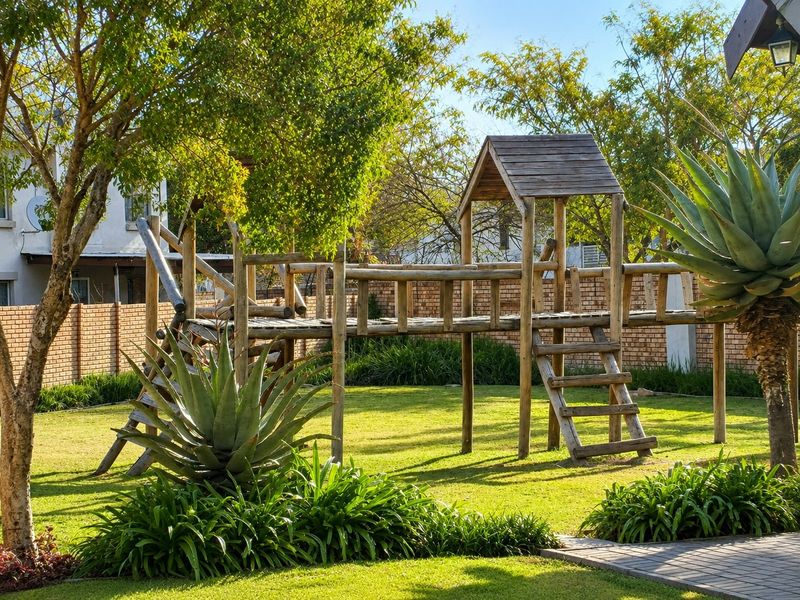 A well-maintained private garden featuring a lush lawn, mature trees, established aloe plants, and a brick boundary wall.