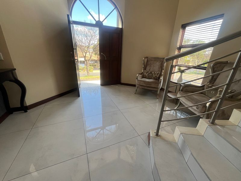 Bright and spacious entrance hall featuring polished large-format floor tiles, a modern stainless steel staircase railing, and an elegant arched front door.