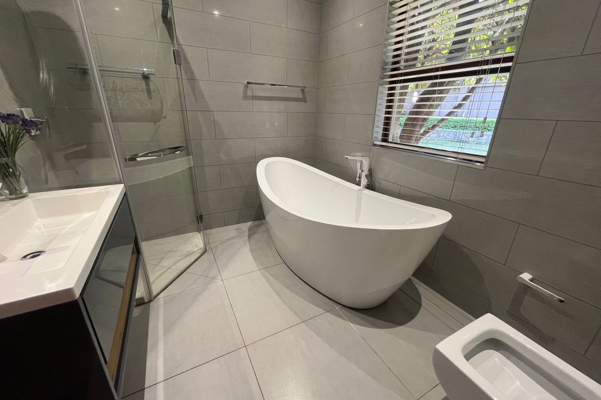 Modern bathroom featuring a sleek freestanding bathtub, glass-enclosed shower, wall-mounted vanity, and bidet, finished with contemporary grey tiling throughout.