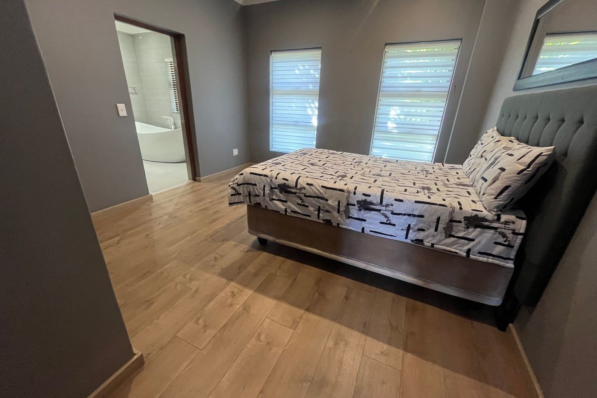 A well-maintained bedroom featuring modern laminate flooring, neutral grey walls, and direct access to an en-suite bathroom with a freestanding tub.