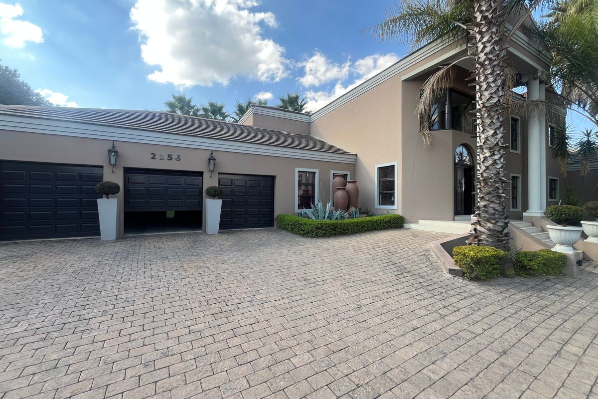 A well-maintained front elevation featuring a paved driveway, double garage, and an elegant entrance with architectural columns.