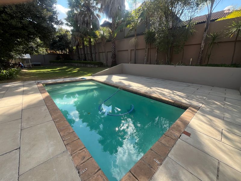 A private swimming pool area featuring a paved surround, boundary wall, and established garden, providing a functional outdoor space for recreation.