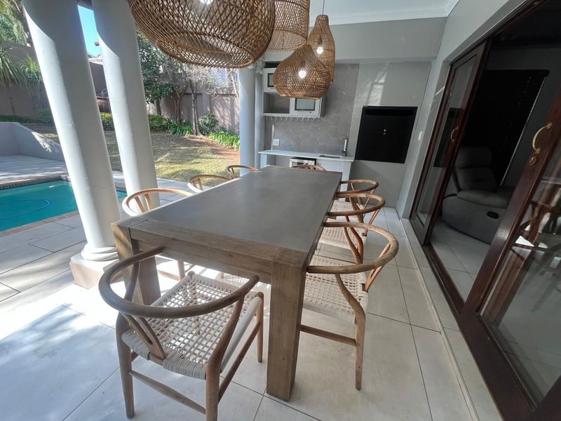 Covered patio featuring a built-in braai, kitchenette with sink, and tiled flooring, overlooking the swimming pool and garden area.