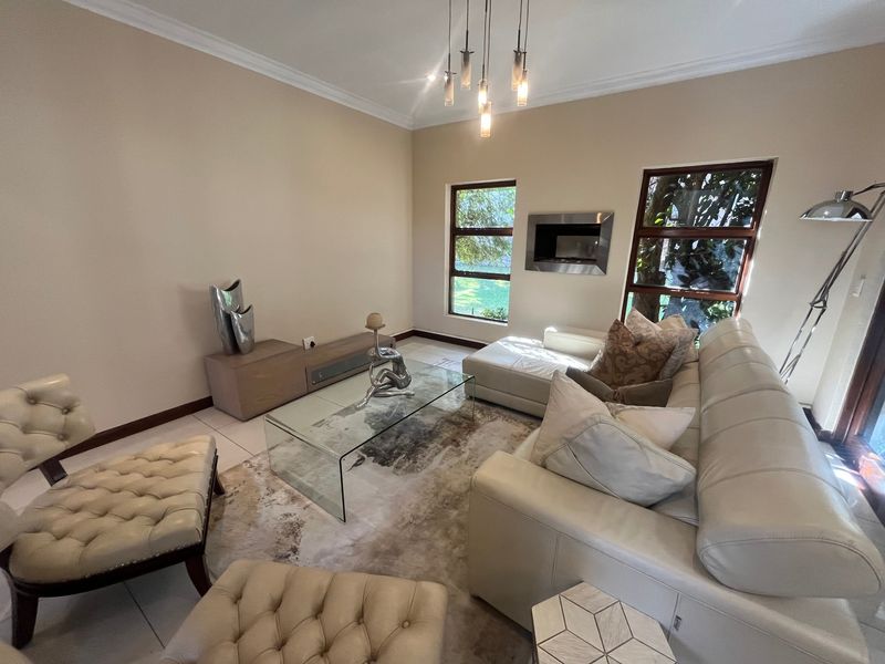 A well-maintained living room featuring a built-in fireplace, tiled flooring, and large timber-framed windows that provide natural light.