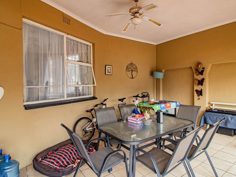 A covered patio area featuring tiled flooring, a ceiling fan, and a large window with security bars, offering a functional outdoor living space.