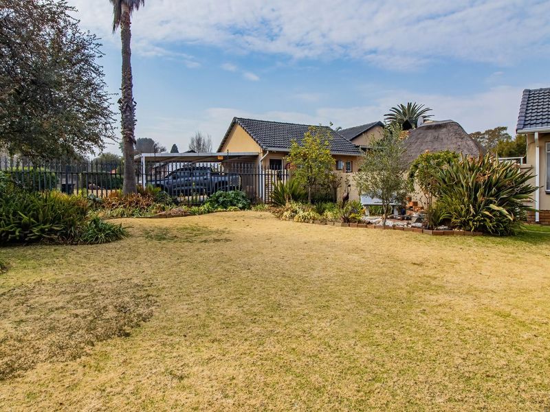 A view of the rear garden featuring a lawn, established landscaping, perimeter fencing, and a carport attached to the main house structure.