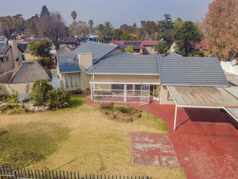 Aerial view of a residential property featuring a tiled roof, covered patio, carport, and a spacious garden with paved driveway areas.