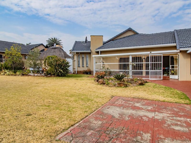 Rear view of the property featuring a paved patio area, security gates, and a spacious garden with established landscaping.