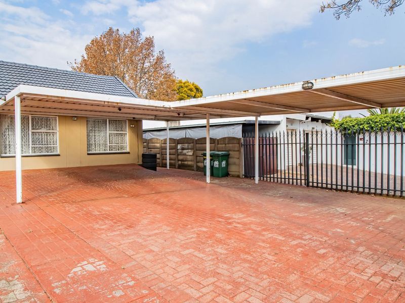 Front exterior view featuring a paved driveway, a large metal carport structure, and secure perimeter fencing.