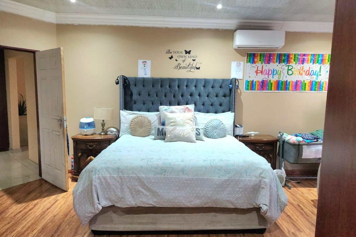 A well-maintained bedroom featuring laminate flooring, recessed ceiling lighting, and a wall-mounted air conditioning unit.