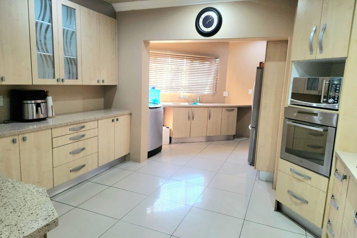 A functional kitchen featuring light wood cabinetry, granite countertops, built-in oven and microwave, and tiled flooring, with an adjoining scullery area.