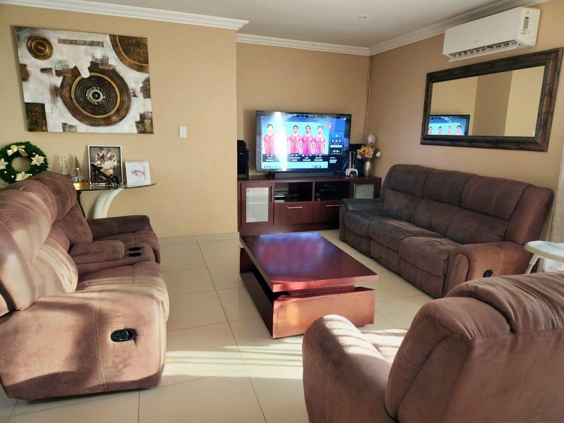 A comfortable living room featuring tiled flooring, coving, and a wall-mounted split-system air conditioner.
