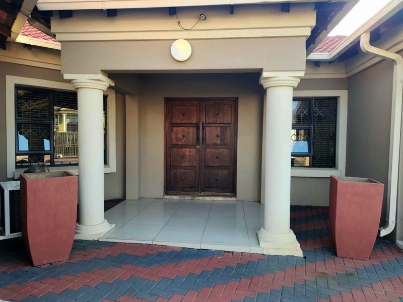A welcoming front entrance featuring a double wooden door, tiled porch area, and decorative columns, complemented by paved exterior flooring.