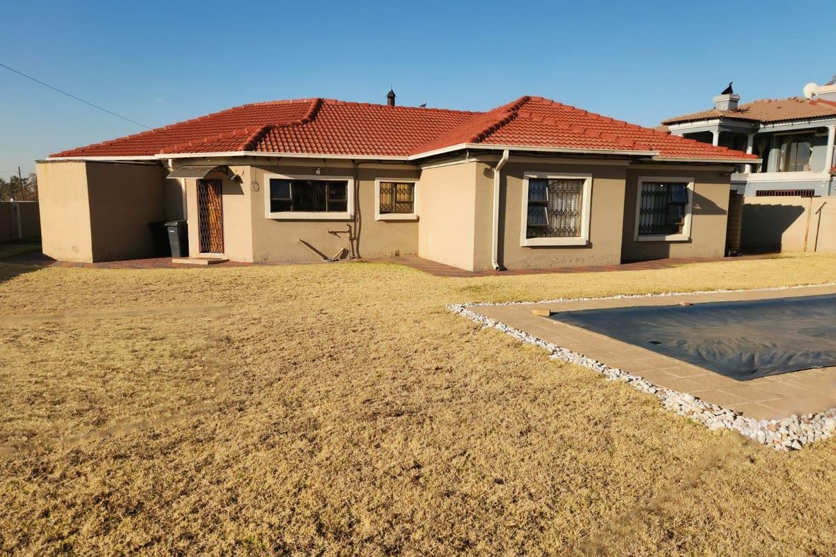 Rear view of the house featuring a tiled roof, paved patio area, and a swimming pool set within a large garden.