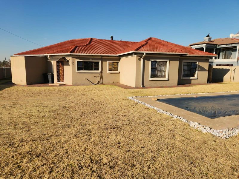 Rear view of the house featuring a tiled roof, paved patio area, and a swimming pool set within a large garden.