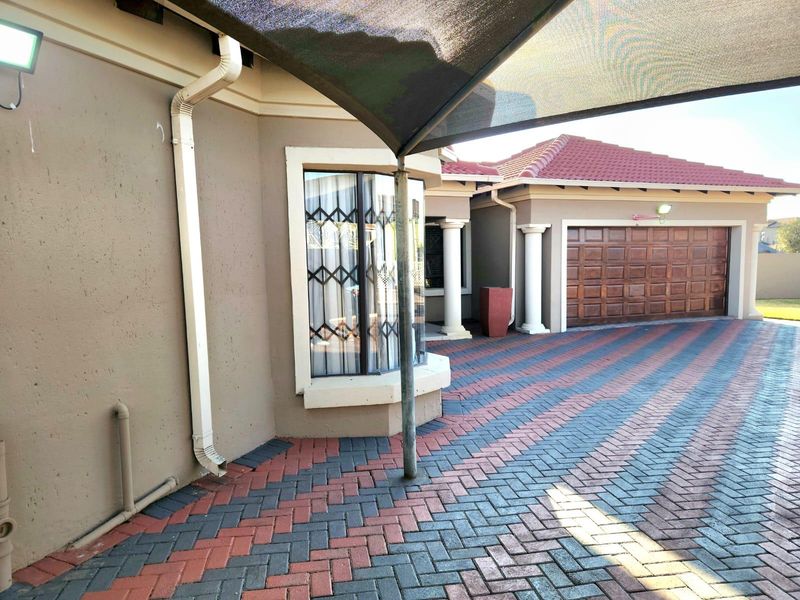 Front exterior view featuring a paved driveway, a wooden garage door, and a bay window with security gates under a shade sail.