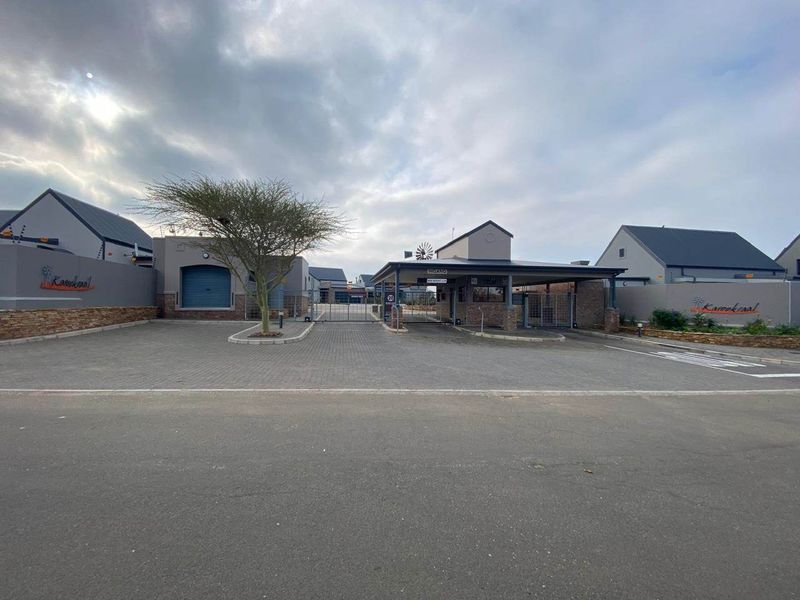 The secure entrance to the Karookraal estate, featuring a paved driveway, guard house, and perimeter walling with electric fencing.