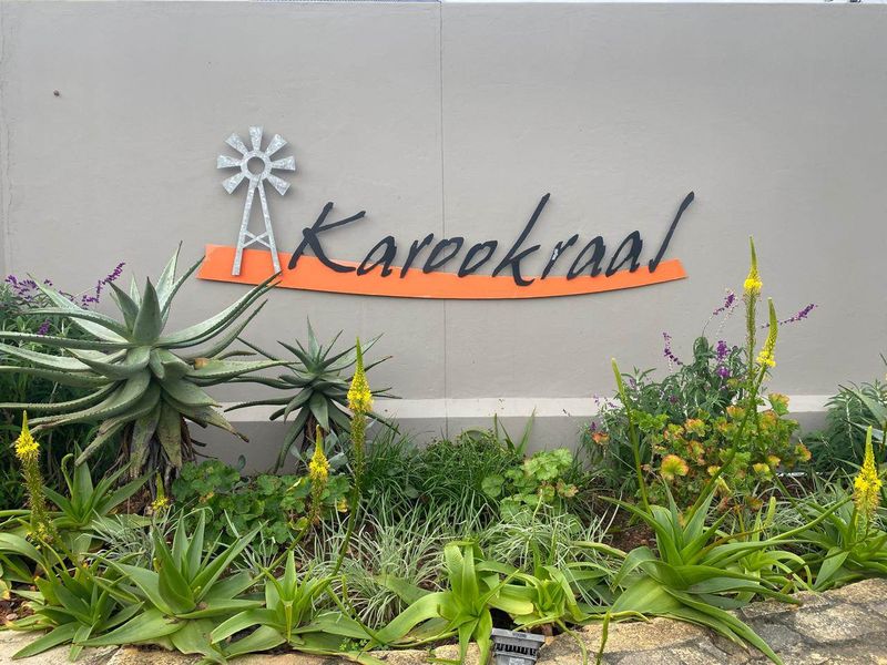 A well-maintained boundary wall featuring the Karookraal estate signage and landscaped garden beds with indigenous plants.