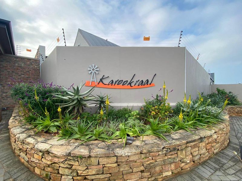 A well-maintained front entrance area featuring a stone retaining wall, landscaped garden, and secure boundary wall with electric fencing.