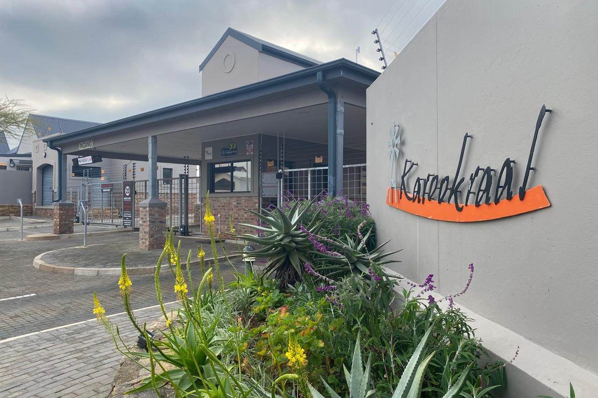 The entrance to the Karookraal estate featuring a secure gated access point, paved driveway, and well-maintained landscaping.