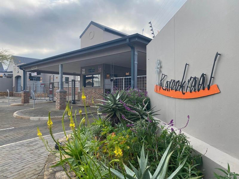 The entrance to the Karookraal estate featuring a secure gated access point, paved driveway, and well-maintained landscaping.