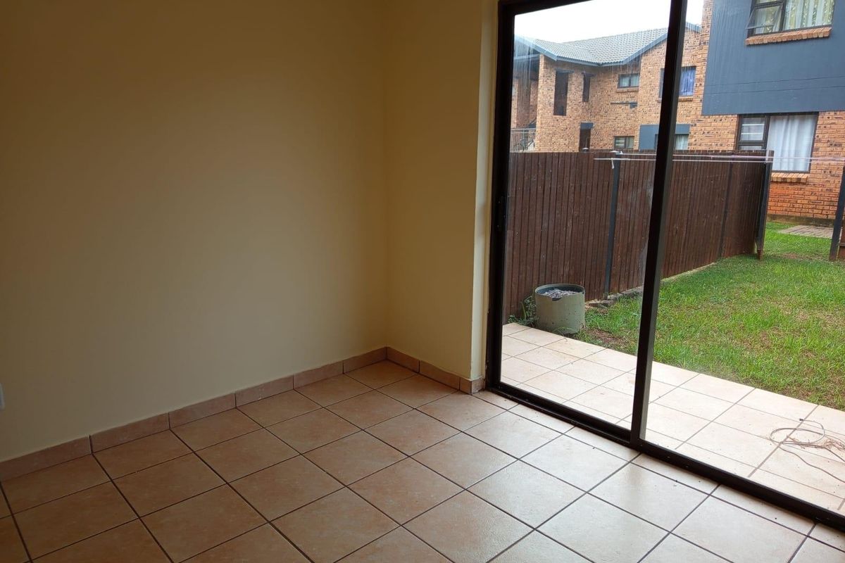 An empty living room featuring ceramic floor tiles and a large sliding glass door providing direct access to the outdoor patio and garden area.